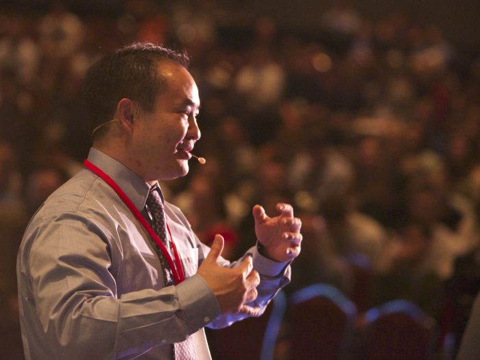 Dennis Yu speaking on stage at a conference